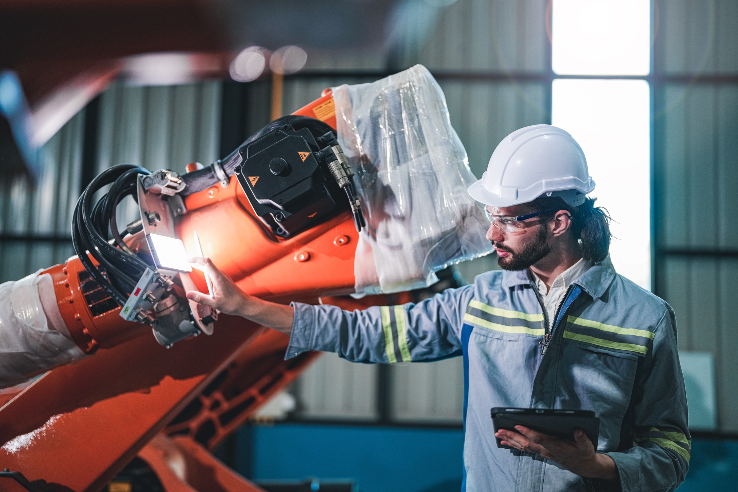Factory engineer reviewing robotic welding operations on a tablet